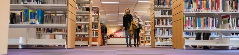 Een paar studenten lopen langs de boekenkasten.