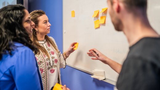 Drie studenten staan bij whiteboard en plakken stickies 