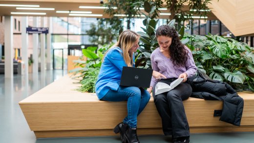 Studenten bespreken lesstof samen op bankje in hoofdgebouw Hogeschool Leiden