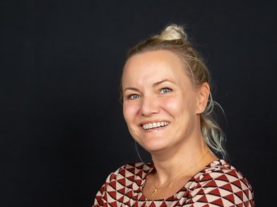 Portret van Marjon, ze heeft haar blonde haar in een knot en een rode top aan
