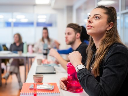 Focusbeeld op luisterende student, met meer studenten in het lokaal