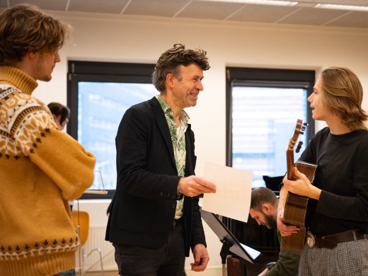 Docent muziek in klas praat met student met gitaar in hand