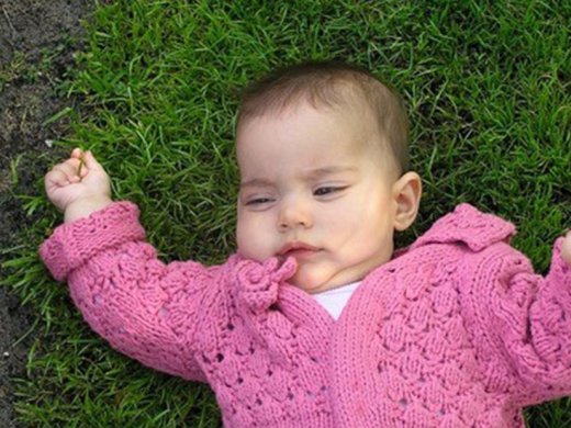 Baby met roze vestje ligt op gras