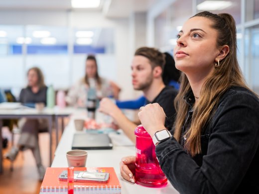 Focusbeeld op luisterende student, met meer studenten in het lokaal