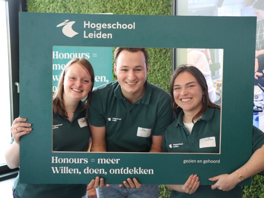 Drie Honoursstudenten houden een bord vast met daarop de tekst: Honours = meer!
