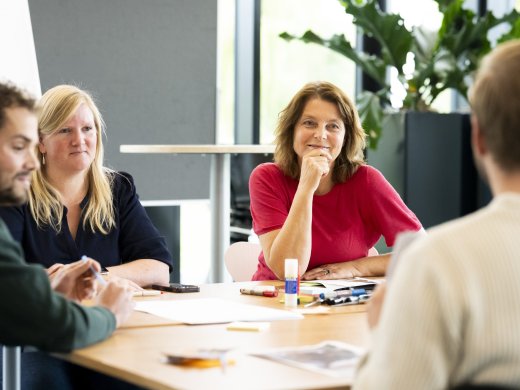 Foto van Arlette Hesselink - Docent Basisvaardigheden Actieonderzoek. Arlette zit aan een ronde tafel met studenten van de cursus.