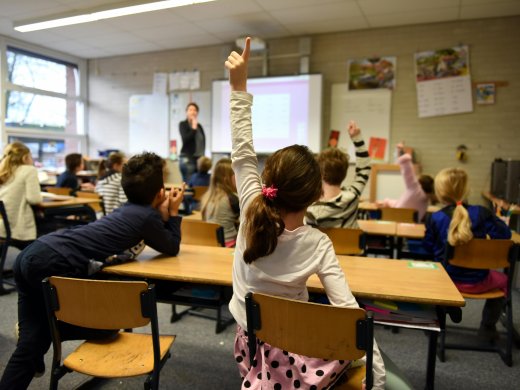 Leerkracht voor de klas, kinderen steken hun vinger op