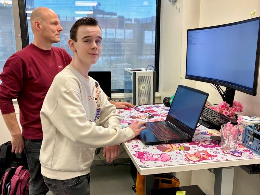 Tom staat samen met Koen aan het bureau