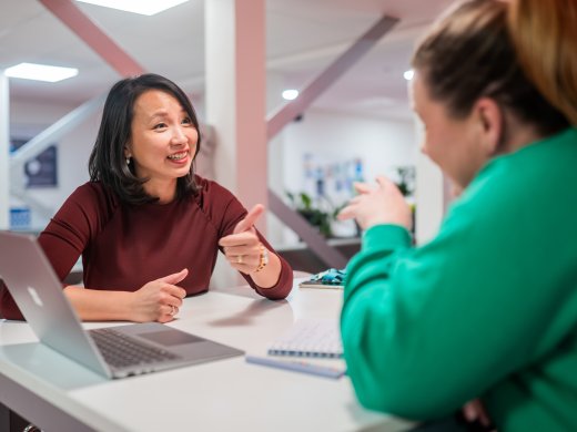 Twee vrouwen zitten aan een tafel met een laptop en praten