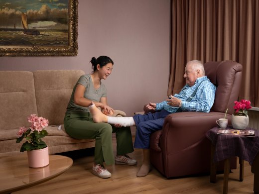 Iemand verbindt het onderbeen van een oudere man, in huiselijke setting