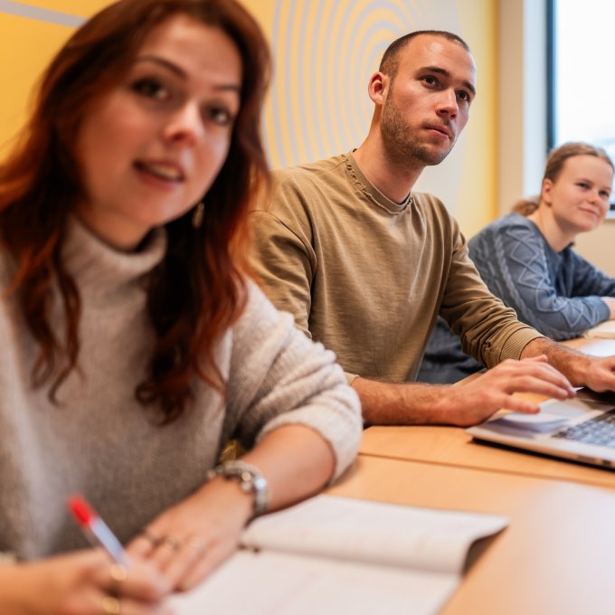 Meerdere studenten van Hogeschool Leiden luisteren en schrijven of typen mee in de klas