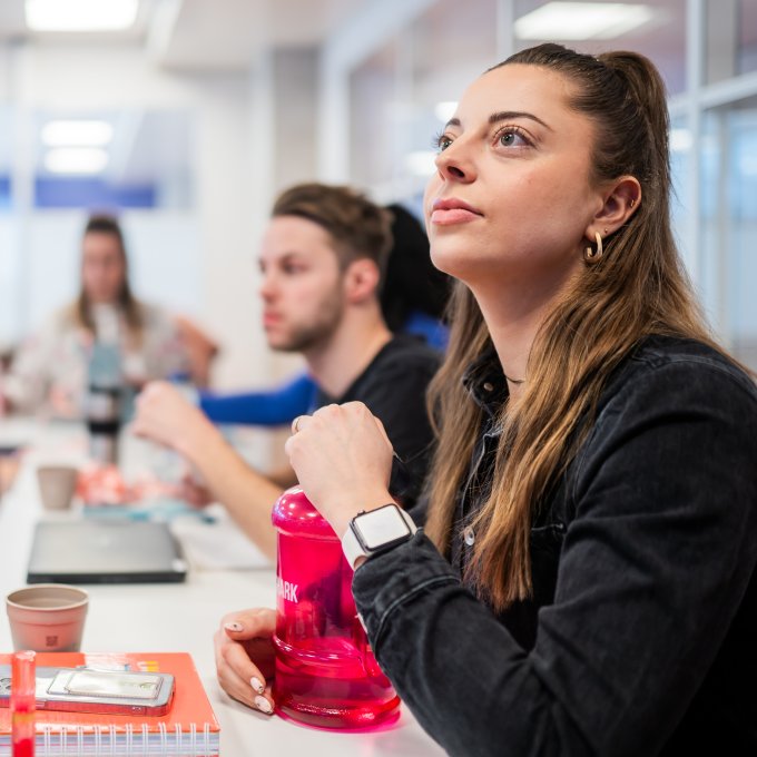 Focusbeeld op luisterende student, met meer studenten in het lokaal