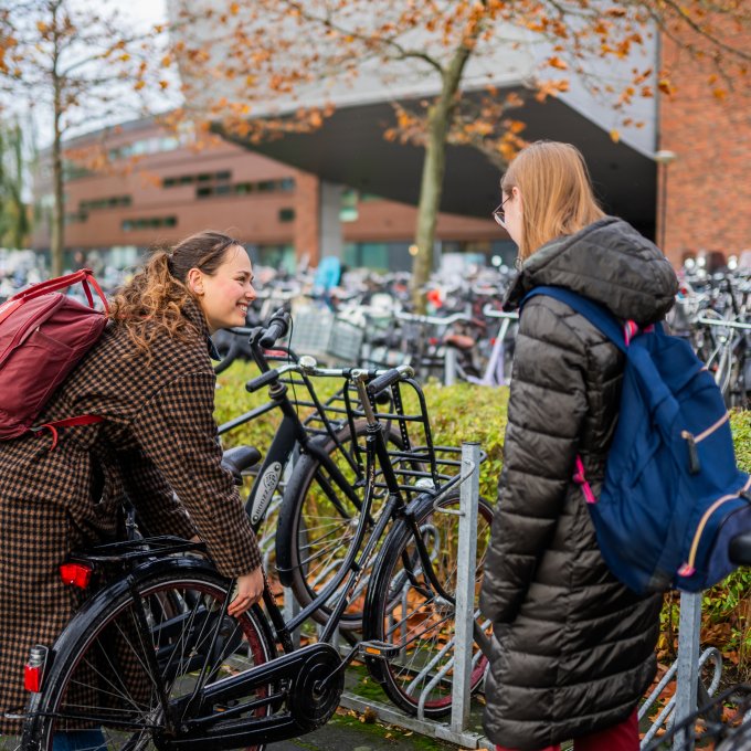 Studenten parkeren fiets bij fietsenstalling voor hoofdgebouw Hogeschool Leiden