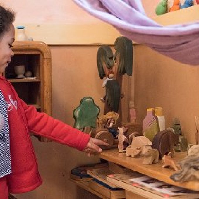 Foto van een kind in een rood outfit die naar houten beeldjes kijkt.