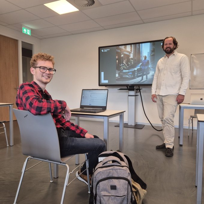 Een docent staat naast een bord met een plaatje gemaakt door Artificial intelligence met een leerling op de tafel ervoor