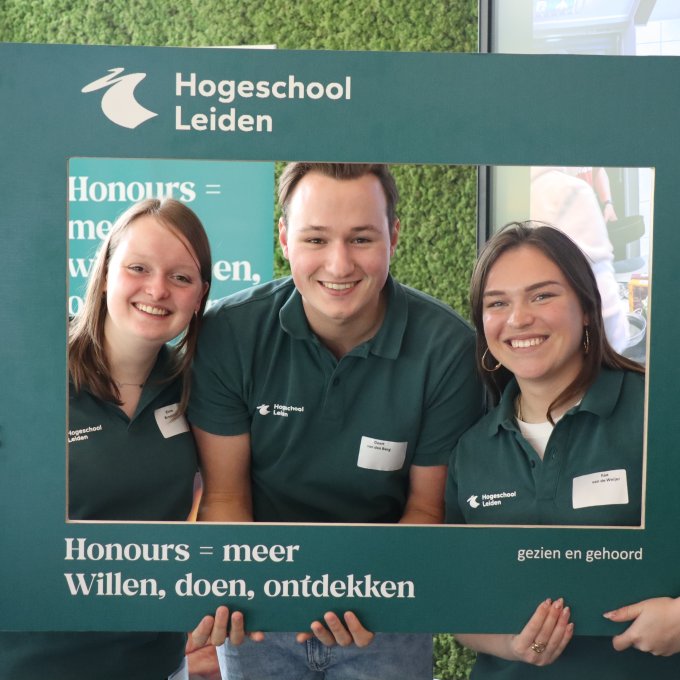 Drie Honoursstudenten houden een bord vast met daarop de tekst: Honours = meer!