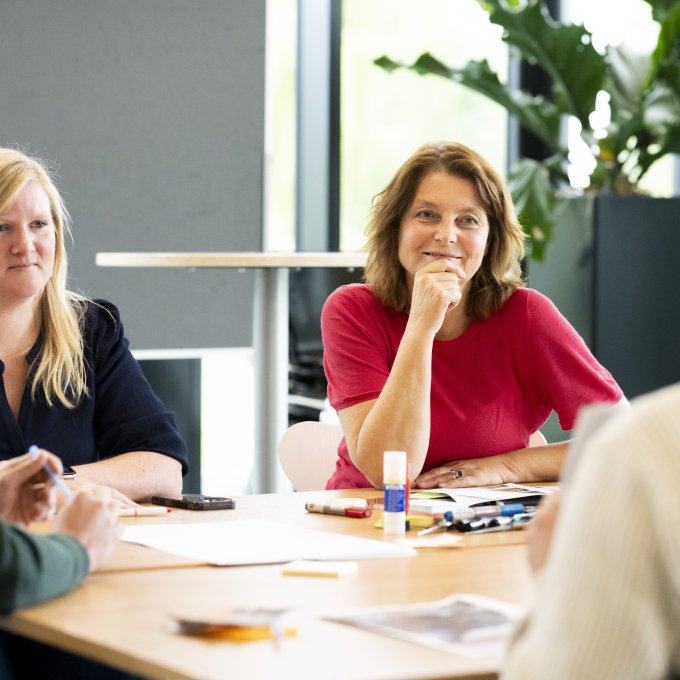 Foto van Arlette Hesselink - Docent Basisvaardigheden Actieonderzoek. Arlette zit aan een ronde tafel met studenten van de cursus.
